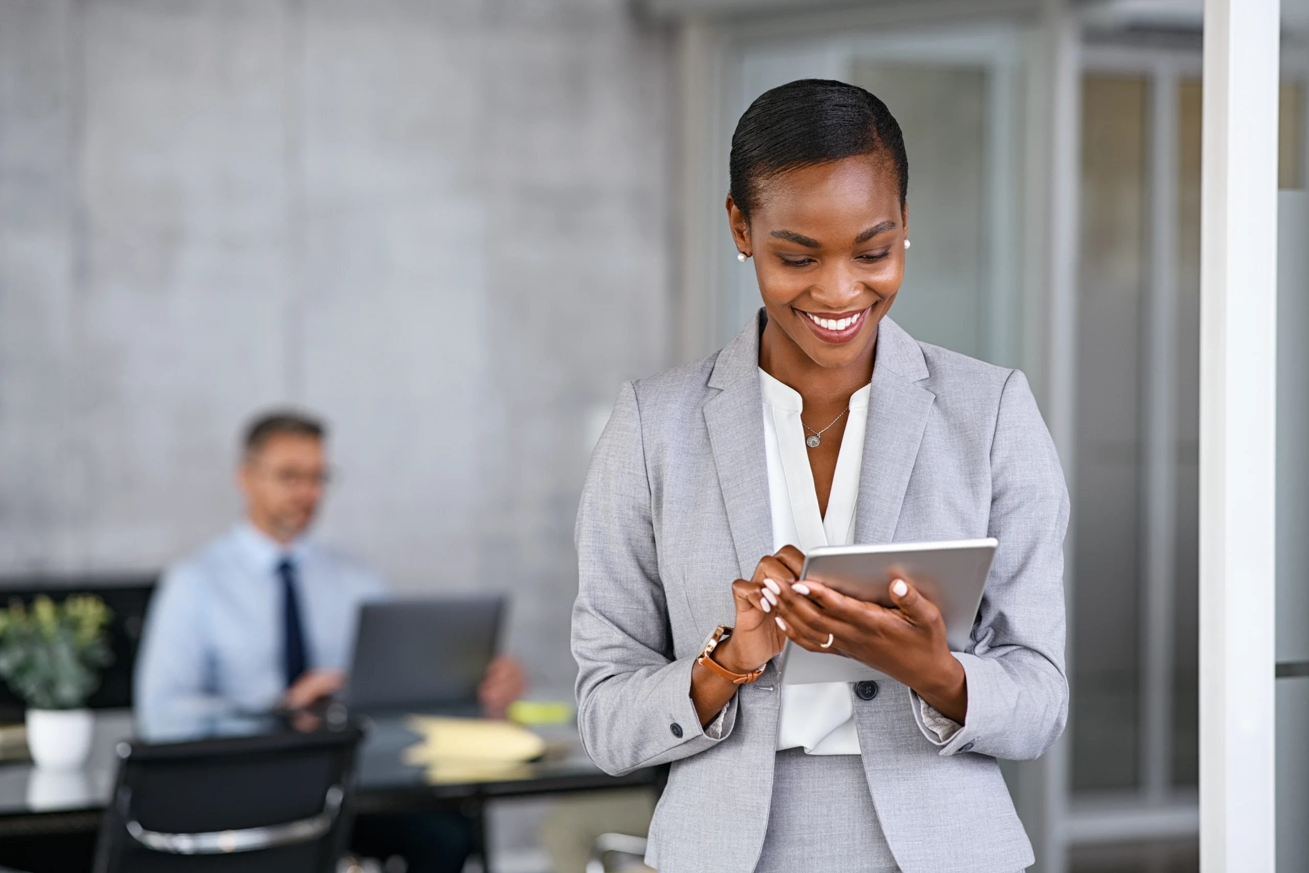 Mature african businesswoman using digital tablet while standing in modern office. Black confident business woman working on digital tablet in meeting room with copy space. Happy successful woman.