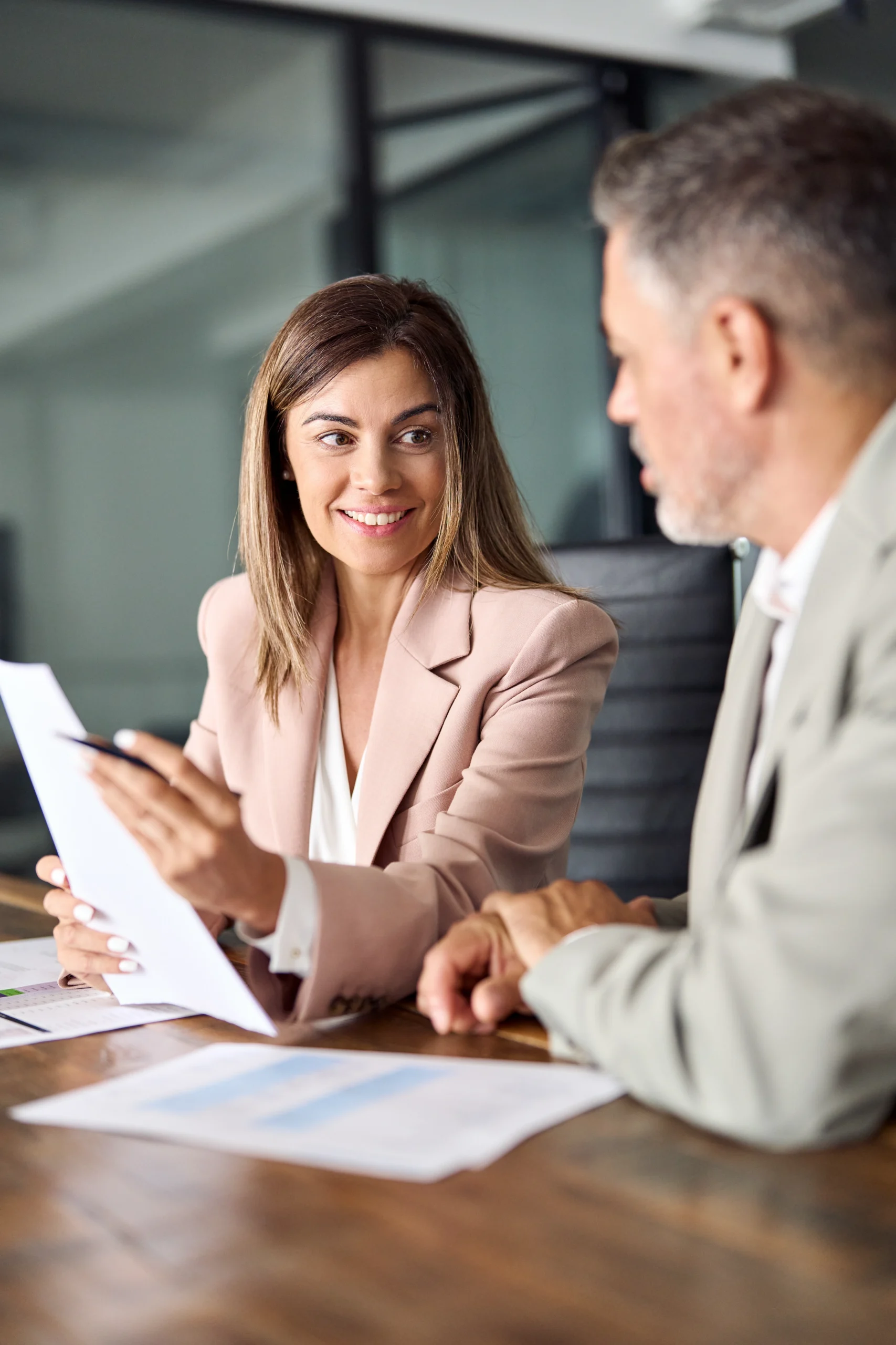 Female lawyer or financial advisor consulting older male client investor showing documents at meeting. Two mature business executive colleagues discussing account paperwork report in office. Vertical