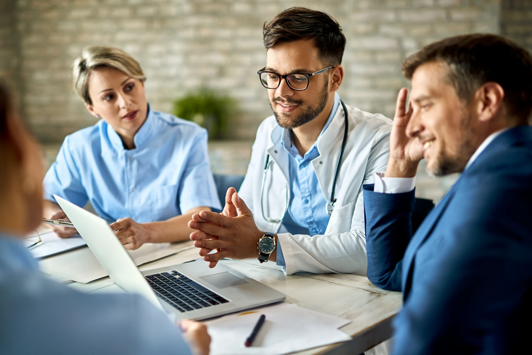 Group of healthcare workers and businessman using laptop while having a meeting in the office. Focus is on young doctor.