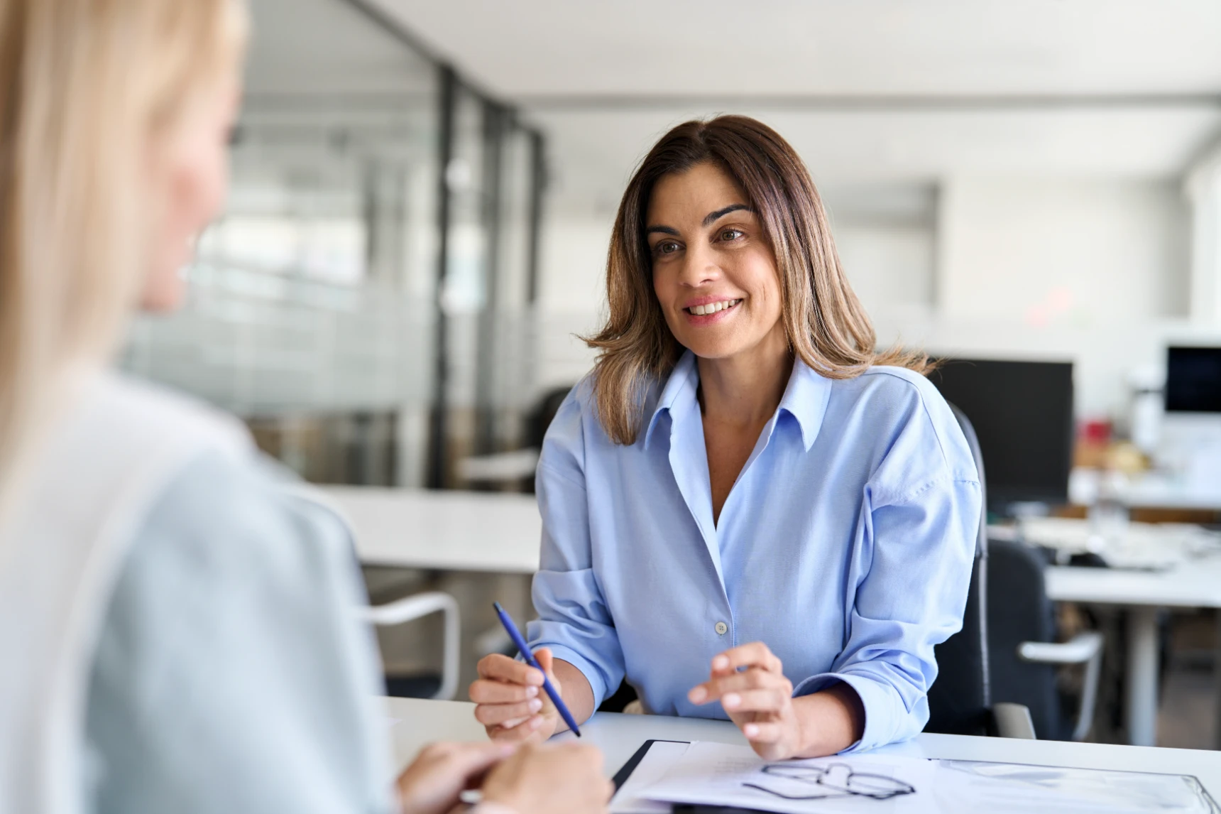 Happy middle aged business woman hr talking to recruit at job interview meeting. Smiling mature female financial advisor, professional bank manager consulting client working in corporate office.